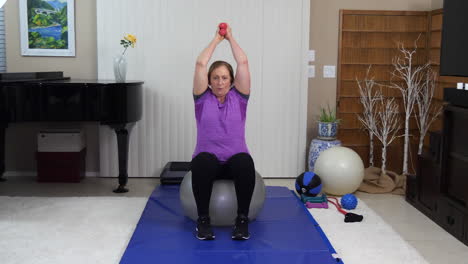 Mature-woman-training-with-dumbbells-working-triceps-while-sitting-on-stability-ball-at-home