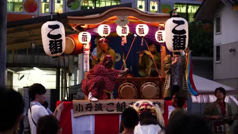Traditional-Japanese-festival-in-the-countryside,-with-a-man-in-a-traditional-lion-costume-dancing-and-interacting-with-the-public,-and-taiko-drums-played-in-the-background