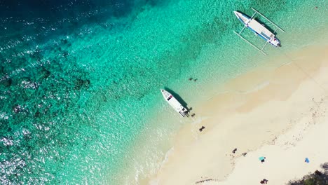 Balinesische-Boote-Transportieren-Touristen-Am-Ufer-Einer-Tropischen-Insel-Mit-Weißem-Sandstrand,-Der-Von-Einer-Türkisfarbenen-Lagune-Umspült-Wird