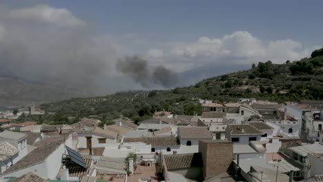Forest-fire-smoking-on-the-edge-of-a-village-with-buildings-and-olive-groves