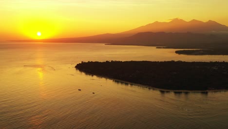 Sun-slowly-dipping-below-the-horizon-across-a-large-body-of-water-with-a-small-island-and-mountains-in-the-background