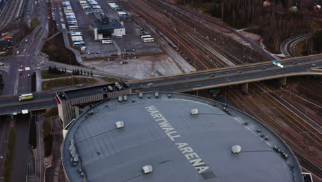 Aerial,-tilt,-drone-shot-over-the-Hartwall-arena,-revealing-the-railway,-on-a-cloudy-day,-in-Pasila,-Helsinki,-Finland