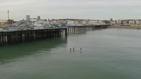 People-riding-paddle-boards-towards-the-shore-in-Brighton-with-pier-and-beach-in-view