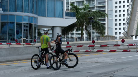 Cyclist-Couple-Waiting-on-Closed-Ramp-in-Front-of-Drawbridge-in-Downtown-Miami-During-Covid-19-Outbreak,-Florida-USA,-50fps