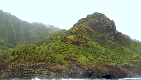 4K-Hawaii-Kauai-Boating-on-ocean-floating-left-to-right-past-rocky-shoreline-toward-cave-with-mountain-in-cloudy-distance