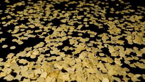 Closeup-of-yellow-confetti-paper-particles-fall-from-above-on-black-table