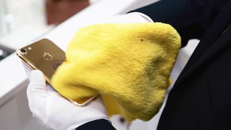 Hands-With-White-Gloves-Cleaning-A-Gold-Plated-Donald-Trump-iPhone-7-Using-A-Yellow-Cloth---high-angle-shot