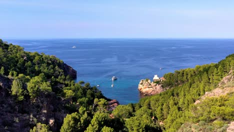 Cala-Deia-in-Mallorca-Spain-with-white-yacht-stationed-by-the-cove,-Aerial-pedestal-up-shot