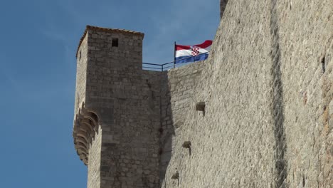 View-of-the-Croatian-flag-blowing-on-top-of-a-watch-tower-along-the-wall-at-old-town-Durbrovnik,-Croatia