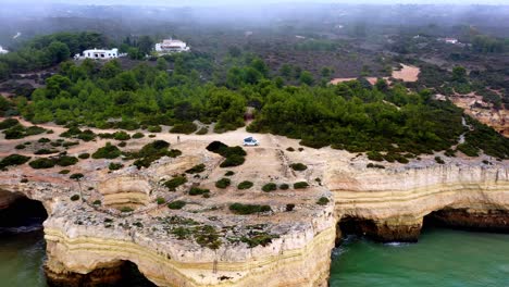 Fontainhas-Beach-sea-carved-caves-in-Portugal-with-camping-van-on-top,-Aerial-dolly-in-reveal-shot