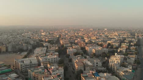 Luftaufnahme-über-Wohngebäude-In-Karatschi-Bei-Sonnenuntergang-Mit-Vorbeifliegenden-Vögeln