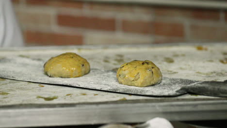 Baker-Placing-Raisin-Bread-Cookie-Dough-Brushed-With-Egg-Wash-On-A-Baking-Peel---close-up