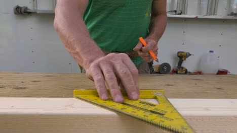 A-carpenter-seen-putting-a-piece-of-wood-on-table-and-marking-a-45-degree-angle-onto-it-using-a-square
