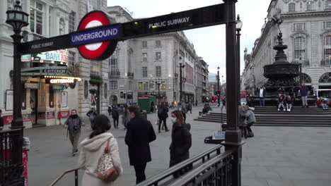 A-woman-wearing-a-surgical-face-mask-descends-with-another-person-into-an-Underground-Station-at-an-empty-Piccadilly-Circus