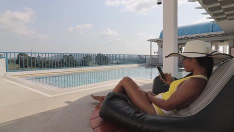 A-beautiful-woman-relaxing-on-a-beanbag-by-the-pool-in-a-hotel-in-Pattaya,-Thailand---wide-shot