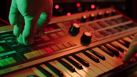 slow-motion-shot-of-a-man-playing-keys-and-turning-knobs-on-a-vintage-synth,-red-and-green-mood