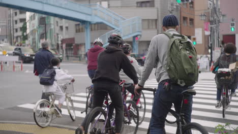 People-Riding-Bicycles-Crossing-Across-The-Urban-Road-In-Tokyo,-Japan