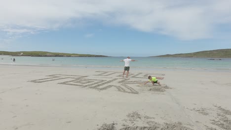 Man-Writing-Tik-Tok-On-The-Beach-Sand-By-His-Foot,-Waves-Washed-The-Sand-Writing-At-The-Dog's-Bay-Beach-In-Connemara,-Ireland-On-A-Summer-Day---timelapse