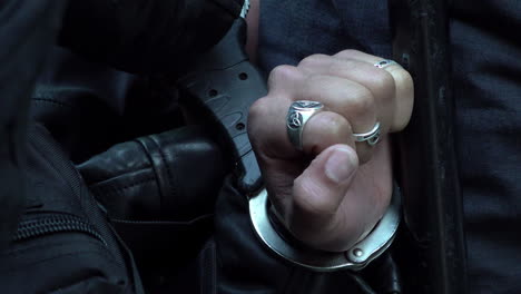 Polizisten-Mit-Schwarzen-Lederhandschuhen-Fesseln-Eine-Person-Mit-Schnellhandschellen,-Deren-Hände-Mit-Silbernen-Ringen-An-Den-Fingern-Zu-Sehen-Sind