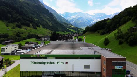 Aerial-shot-flying-backwards-revealing-Elmer-mineral-water-plant-in-Elm,-Glarus,-Switzerland