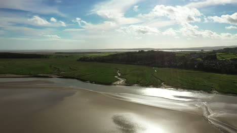 Aerial-view-of-a-coastal-bay-at-low-tide-with-sun-shimmering-on-the-golden-sand,-bright-summers-day