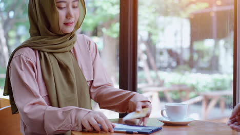 Junge-Schöne-Asiatische-Muslimische-Frauen-Genießen-Einen-Entspannten-Moment-Beim-Arbeiten-Und-Spielen-Mit-Dem-Mobiltelefon-Im-Café-An-Einem-Strahlend-Sonnigen-Tag