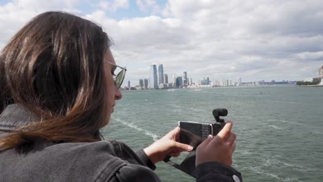 Nahaufnahme-Einer-Jungen-Frau,-Die-Mit-Ihrem-Smartphone-Von-Der-Staten-Island-Ferry-Aus-Videos-Von-Der-New-Yorker-Küste-Aufnimmt