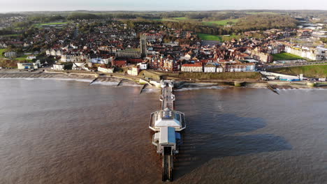 Drone-footage-from-the-sea-flying-over-the-pier-at-Cromer,-Norfolk-towards-the-town-in-early-morning