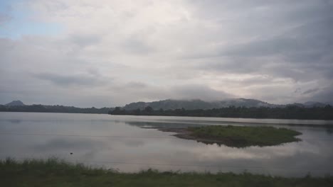 Driving-by-a-calm-misty-lake-with-mountains-in-the-background