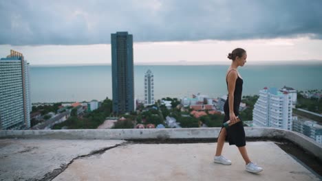 Shot-of-young-woman-in-black-dress-walking-on-roof-with-a-sea-view-and-looking-front