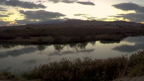 Time-lapse-of-a-sunset-reflecting-off-the-smooth-surface-of-a-river-then-zooming-out-to-reveal-a-wide-angle-scene