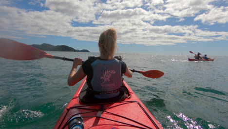 Beautiful-blonde-woman-in-a-red-canoe-is-paddling-over-the-ocean-in-Abel-Tasman-Nationalpark-in-New-Zealand