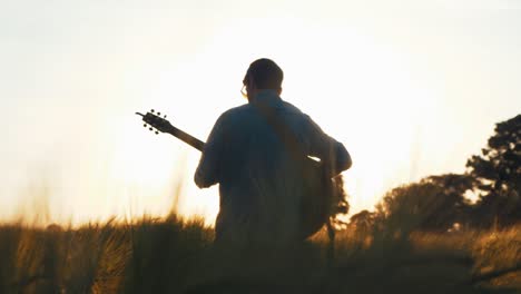 Musiker-Im-Feld-Während-Des-Sonnenuntergangs,-Der-Gitarre-Spielt