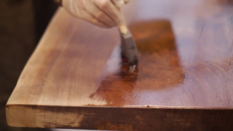 A-craftsman-is-finishing-a-custom-hand-made-natural-wood-table-top-with-a-coat-of-varnish-in-his-wood-shop