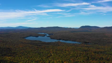 Aerial-drone-establishing-shot-over-a-calm-blue-forest-lake-with-the-thick-green-and-autumn-colored-forest-into-the-distance-of-the-Maine-wilderness-in-early-fall