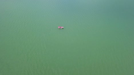 Aerial-Approach-shot-of-lake-with-boat-floating-in-the-middle,-top-down-shot