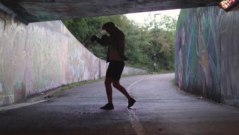Wide-Shot-of-a-Young-Athletic-Man-Boxing-in-an-Underpass,-Silhouetted-By-The-Light-Behind-Him