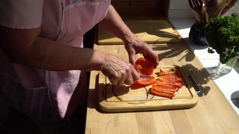 Senior-lady-cutting-paprika-in-the-kitchen-on-a-sunny-afternoon