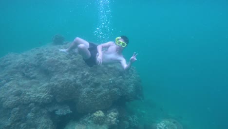 Underwater-shot-of-an-asian-teenager-wearing-snorkle-mask-dive-in-the-sea-and-pose-at-the-camera,-then-swim-up-to-the-surface