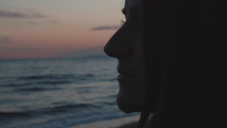 Extreme-close-up-of-a-girl-standing-on-the-beach,-looking-into-the-ocean-on-the-sunset-and-thinking-about-memories