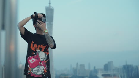 Slow-motion-shot-of-a-young-asian-photographer-capturing-urban-downtown-from-the-rooftop-in-the-early-morning