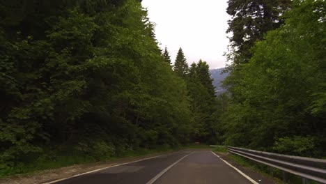 Slow-drive-with-upcoming-traffic-on-a-winding-road-in-a-forest,-Bucegi-mountains,-Romania,-dolly-forward