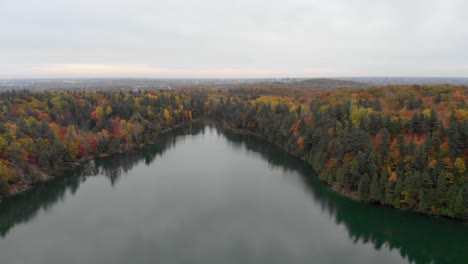 Aerial-footage-over-Pink-Lake-in-Gatineau-Hills-Quebec-going-from-above-the-middle-of-the-lake-to-the-parking-lot-over-a-bike-on-a-curvy-road