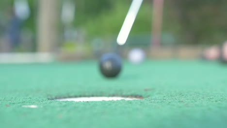 A-Mini-Golf-Player-Putts-and-Gets-the-Golf-Ball-in-the-Hole,-Low-Angle-Slow-Motion,-Shallow-Depth-of-Field