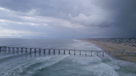 Storm-clouds-and-waves-by-the-Manhattan-Beach-Pier-in-California,-AERIAL-PAN
