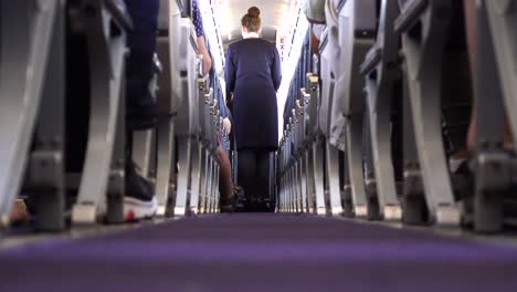 Flight-attendants-serving-passengers-foods-and-drinks-on-airplane,-low-center-aisle-shot,-rows-of-seats-with-passengers