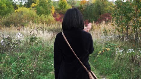 Following-shot-of-girl-walking-through-park-with-autumn-colors-while-swatting-away-flies