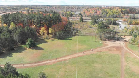 Slow-aerial-footage-facing-down-towards-a-walking-trail-and-power-lines-in-Ottawa,-Ontario-with-hikers-and-a-sunny-autumn-coloured-forest-in-the-distance