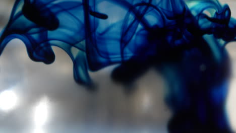Macro-shot-of-a-blue-ink-drop-in-clear-water-as-it-spreads-out-underwater-and-creates-smokey-abstract-shapes-in-the-background