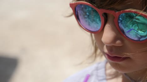 Nahaufnahme-Eines-Süßen-Kleinen-Mädchens-Mit-Sonnenbrille,-Das-Im-Urlaub-Am-Strand-Etwas-Trinkt